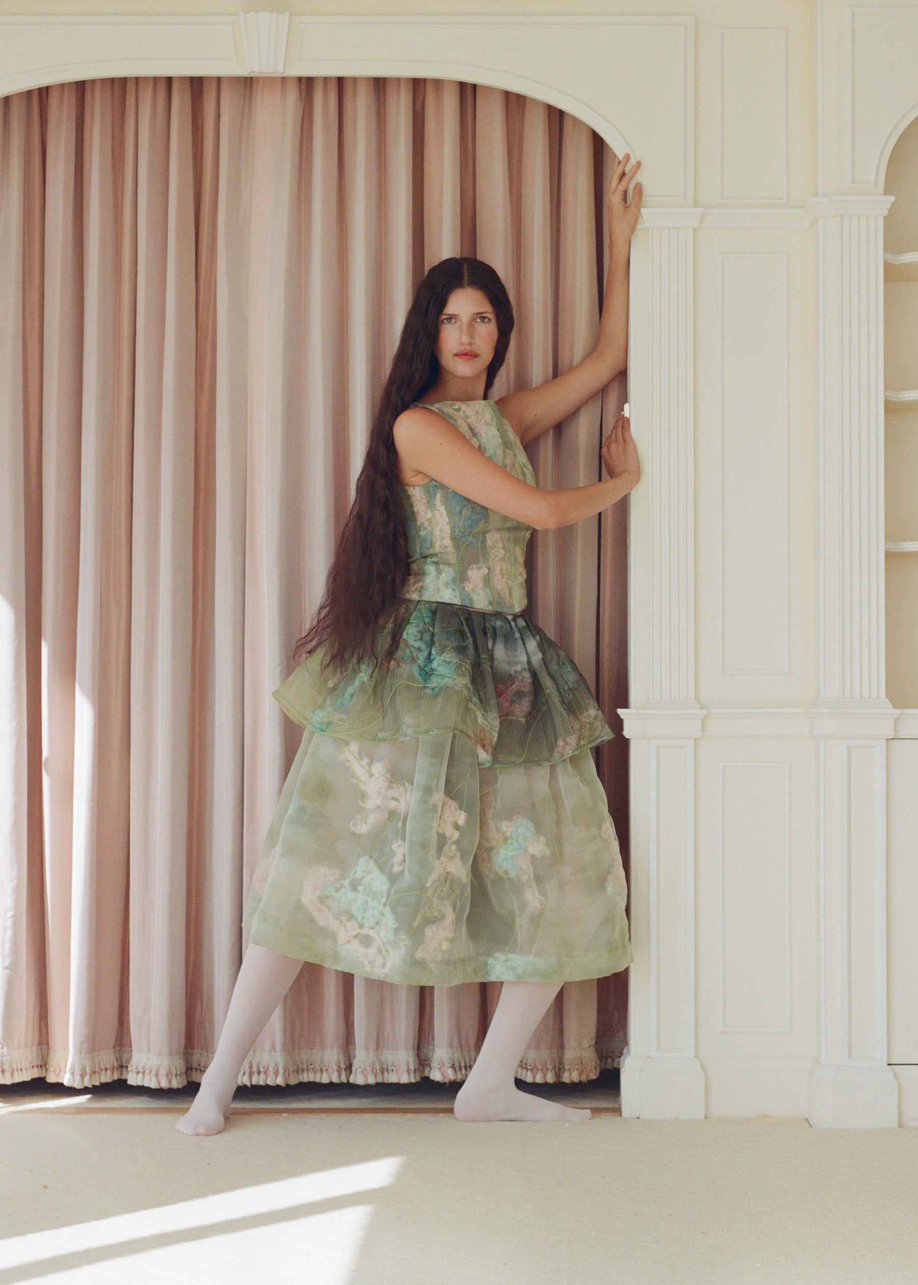 Clara Pinto SS26: a model in a green dress against a pale pink curtain. Photograph by Clara Pinto