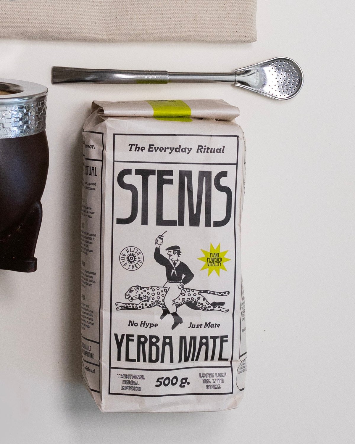 Flatlay of a Stems carton, a leather gourd and a bombilla on a pale ground