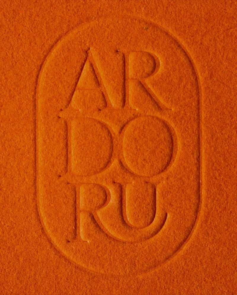ArdorU identity by SR (Studio Riebenbauer): A poised high-contrast serif stacked into a blind-embossed signet on orange stock