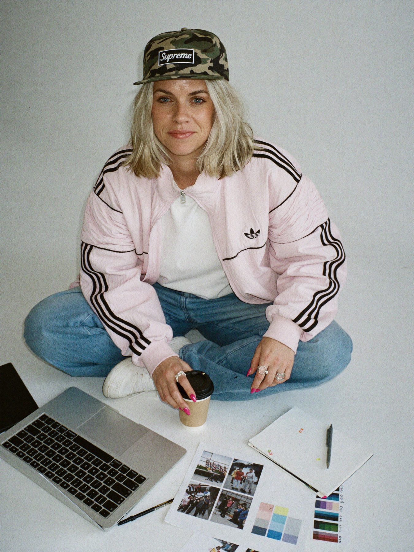 Sophie Evans sitting cross-legged on the studio floor with a laptop, coffee and printed layouts