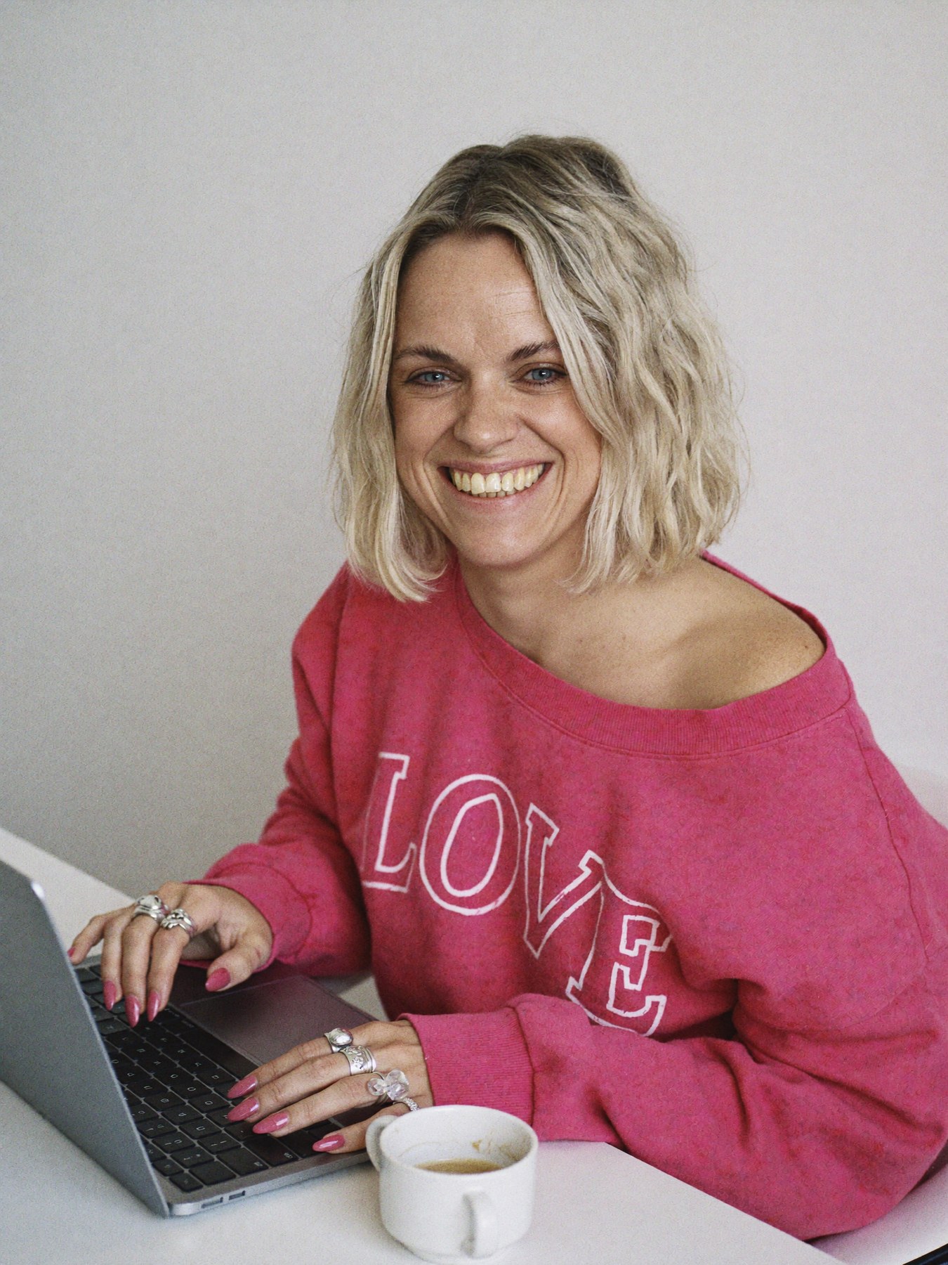 Sophie in a hot pink LOVE sweatshirt, gallery wall and studio details behind her