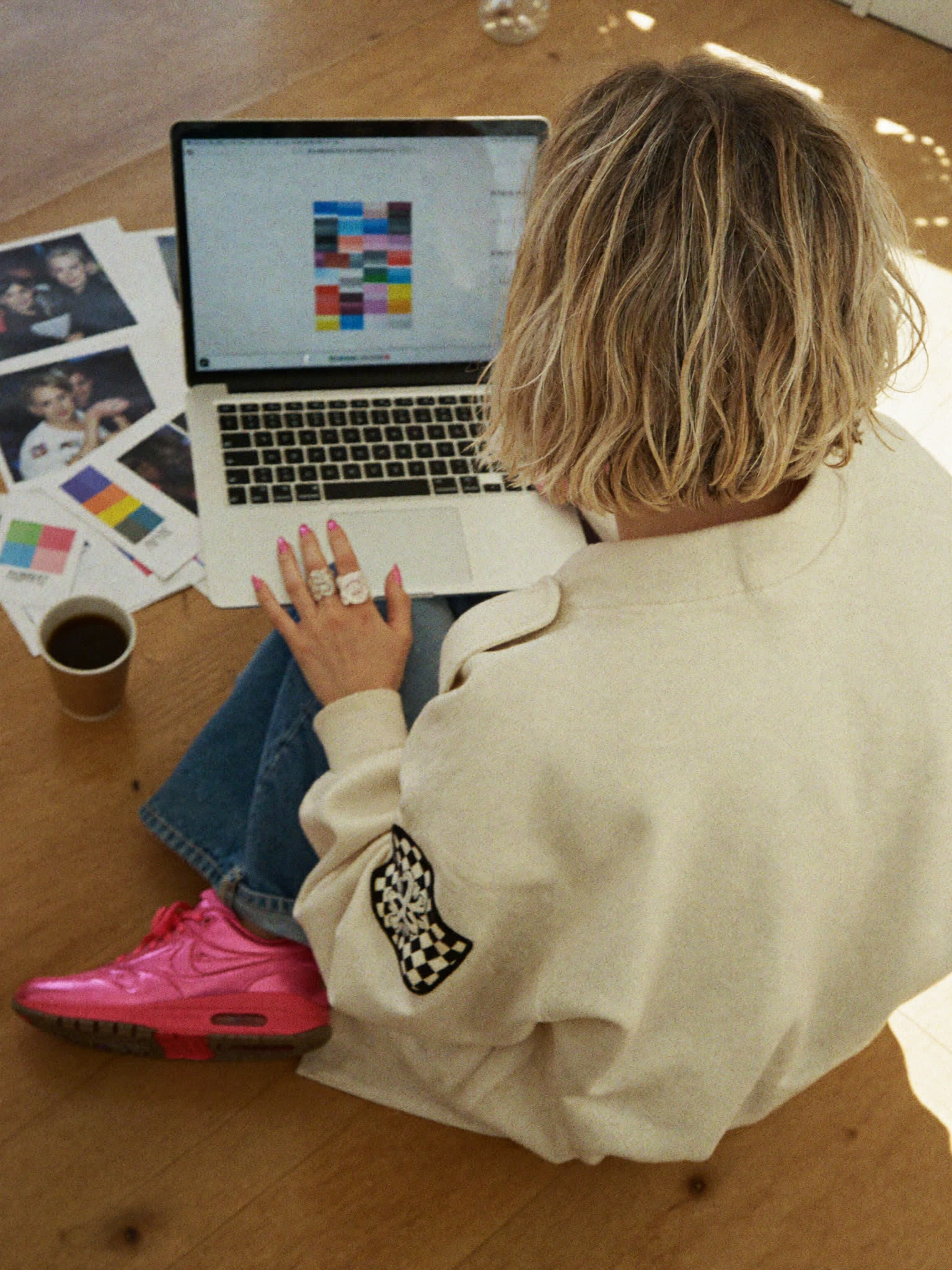 From behind: Sophie Evans on the studio floor with her laptop, a colour grid on screen and prints around her