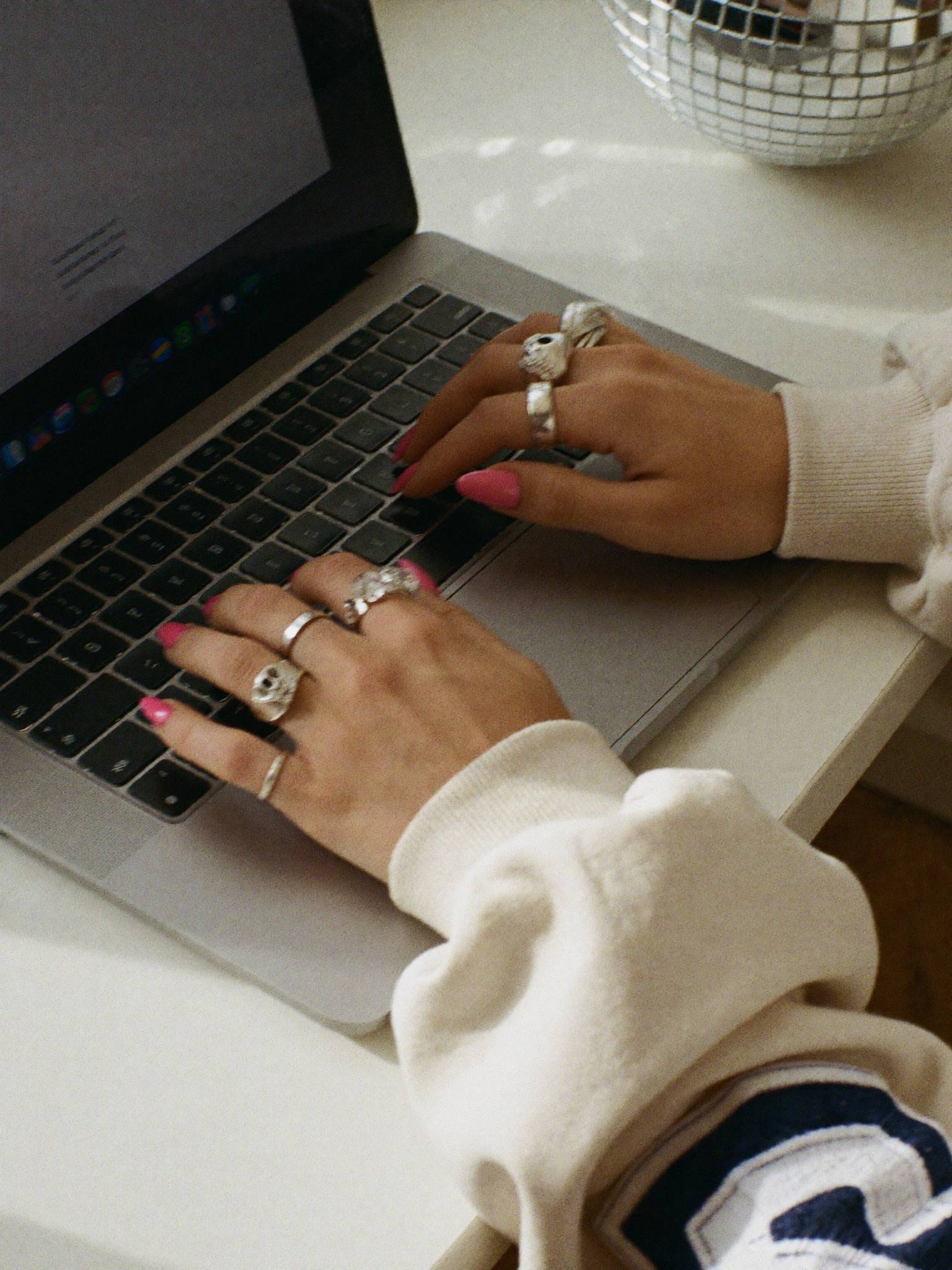 Sophie Evans's hands typing on her laptop, silver rings and pink nails